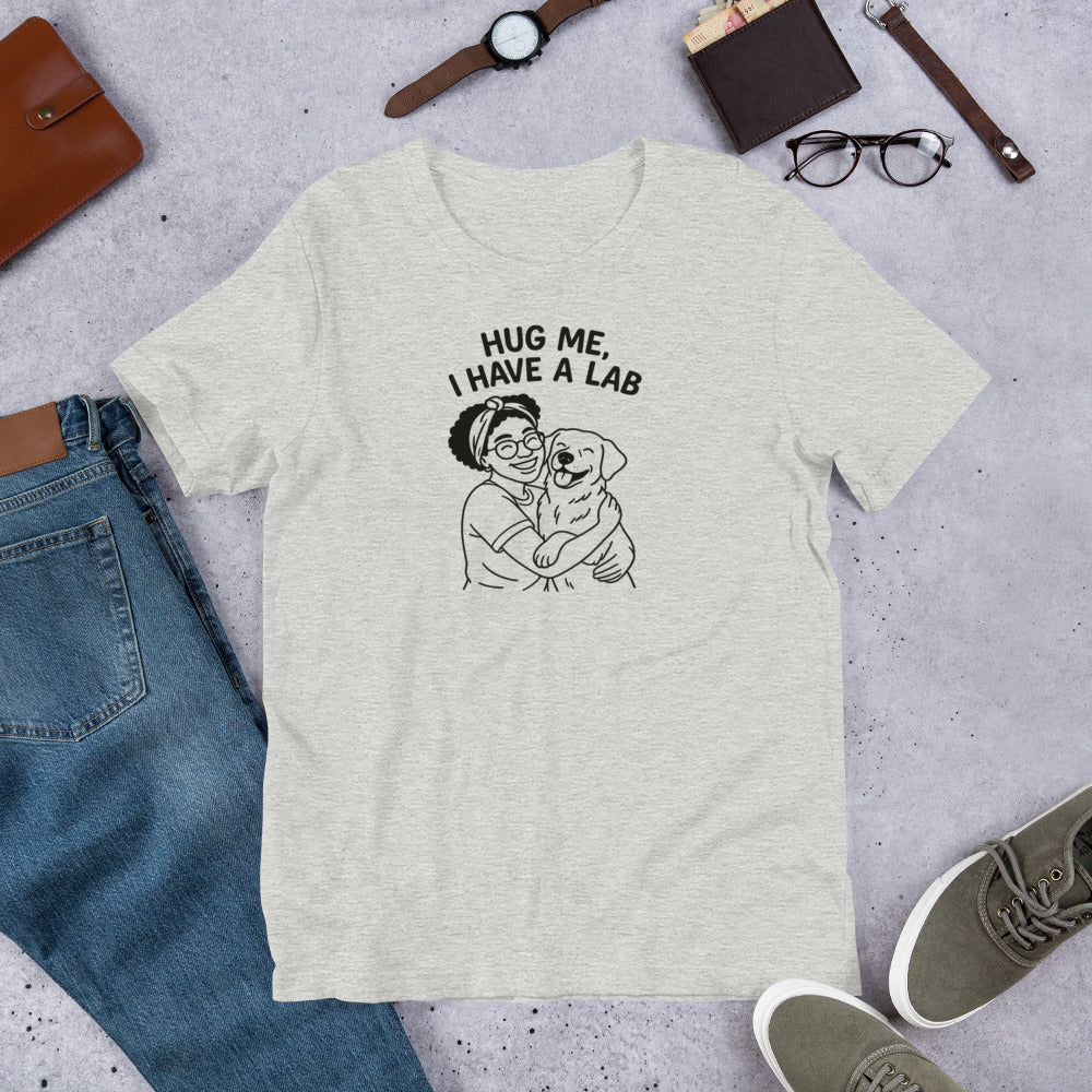 " Hug Me I Have A Lab" - Fun Labrador T-Shirt Gray t-shirt with 'Hug Me, I Have a Lab' graphic on a concrete surface with jeans and shoes.