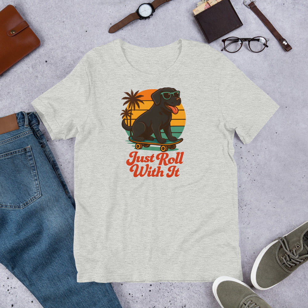 "Just Roll With It" - Black Labrador – Fun Labrador T-Shirt Gray t-shirt with a dog on a skateboard graphic and 'Just Roll With It' text, surrounded by jeans, shoes, and accessories.