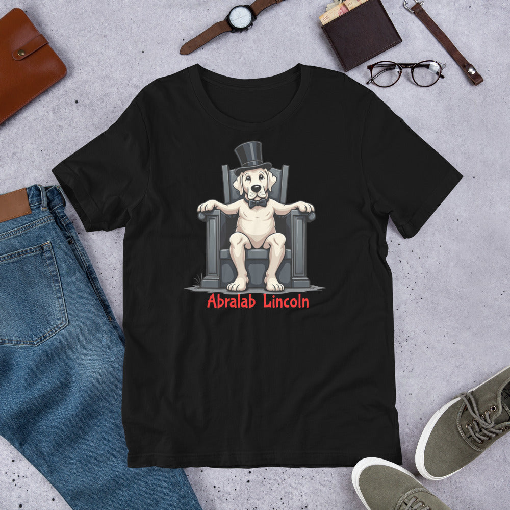 Black t-shirt with a dog wearing a top hat and bow tie on a throne graphic, surrounded by jeans, shoes, and accessories. T-shirt with bold black text that says “Abralab Lincoln,” styled flat with jeans, shoes, and a hat. A playful Labrador lover shirt and perfect gift for Labrador owners who appreciate humor.