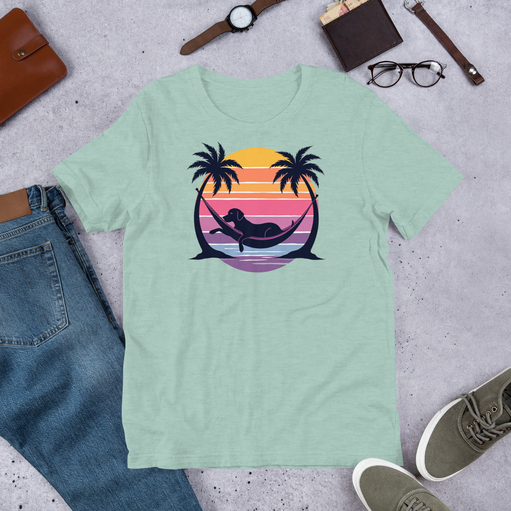"Labrador In Paradise " – Fun Labrador T-Shirt Light green t-shirt with a colorful graphic of a sunset, palm trees, and a mermaid on a gray surface with jeans, shoes, and accessories.