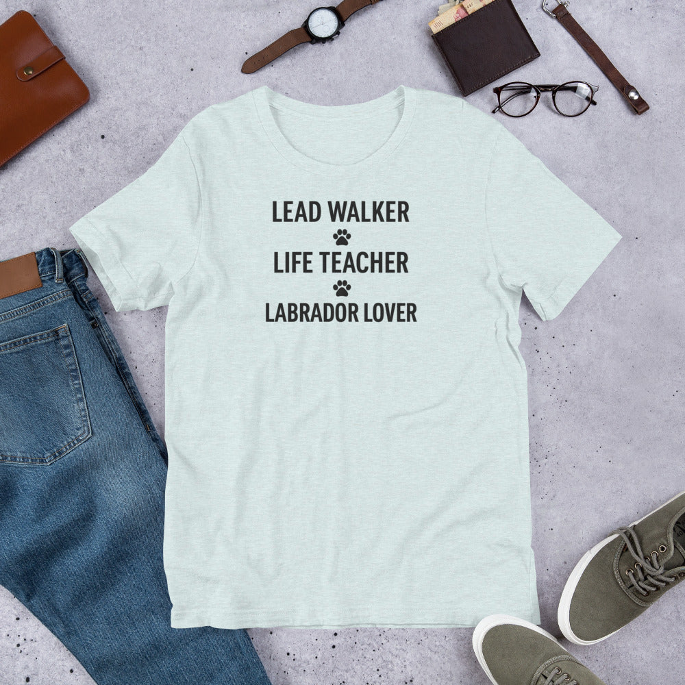 T-shirt with black text that reads 'Lead Walker, Life Teacher, Labrador Lover' with small paw print icons, laid out flat with jeans, sneakers, and accessories.