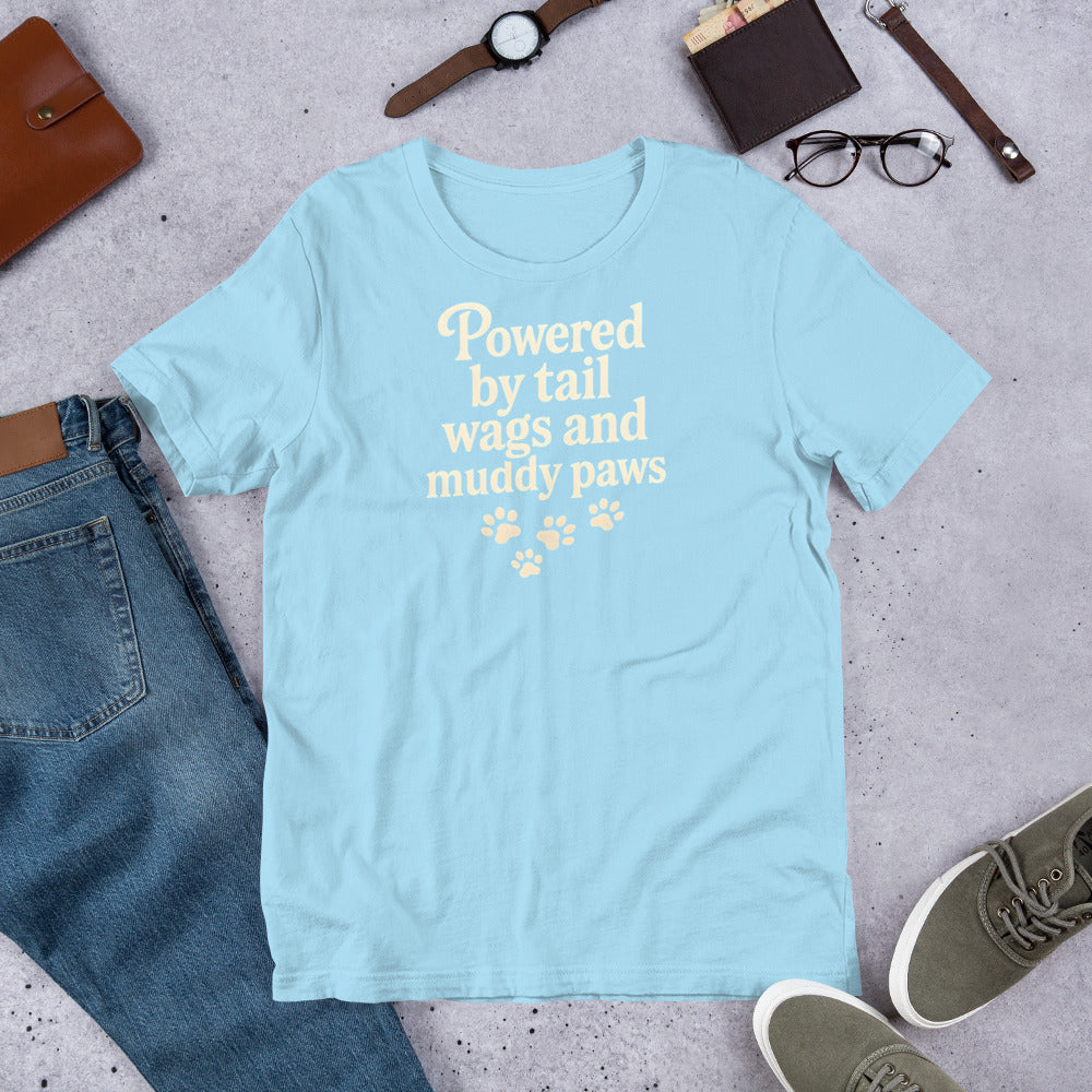 "Powered By Tail Wags And Muddy Paws" - Fun Labrador T-Shirt Light blue t-shirt with text 'Powered by tail wags and muddy paws' on a concrete surface with jeans, shoes, and accessories.