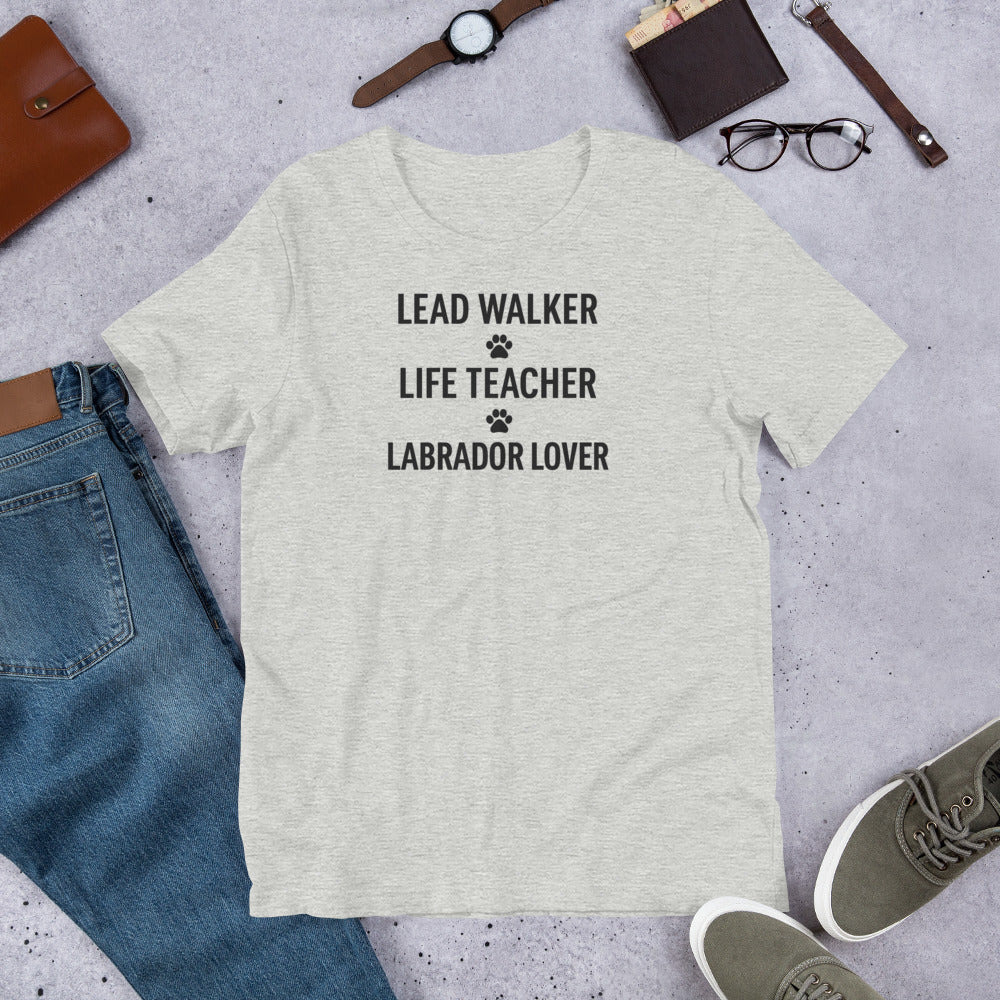 T-shirt with black text that reads 'Lead Walker, Life Teacher, Labrador Lover' with small paw print icons, laid out flat with jeans, sneakers, and accessories.