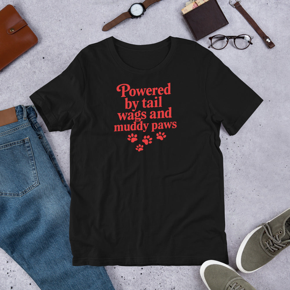 "Powered By Tail Wags And Muddy Paws" - Fun Labrador T-Shirt Black t-shirt with red text and paw prints on a concrete surface with jeans, shoes, and accessories.