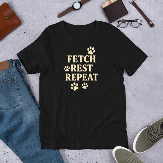 "Fetch Rest Repeat" - Fun Labrador T-Shirt Black t-shirt with 'Fetch Rest Repeat' text on a concrete surface with casual items around.