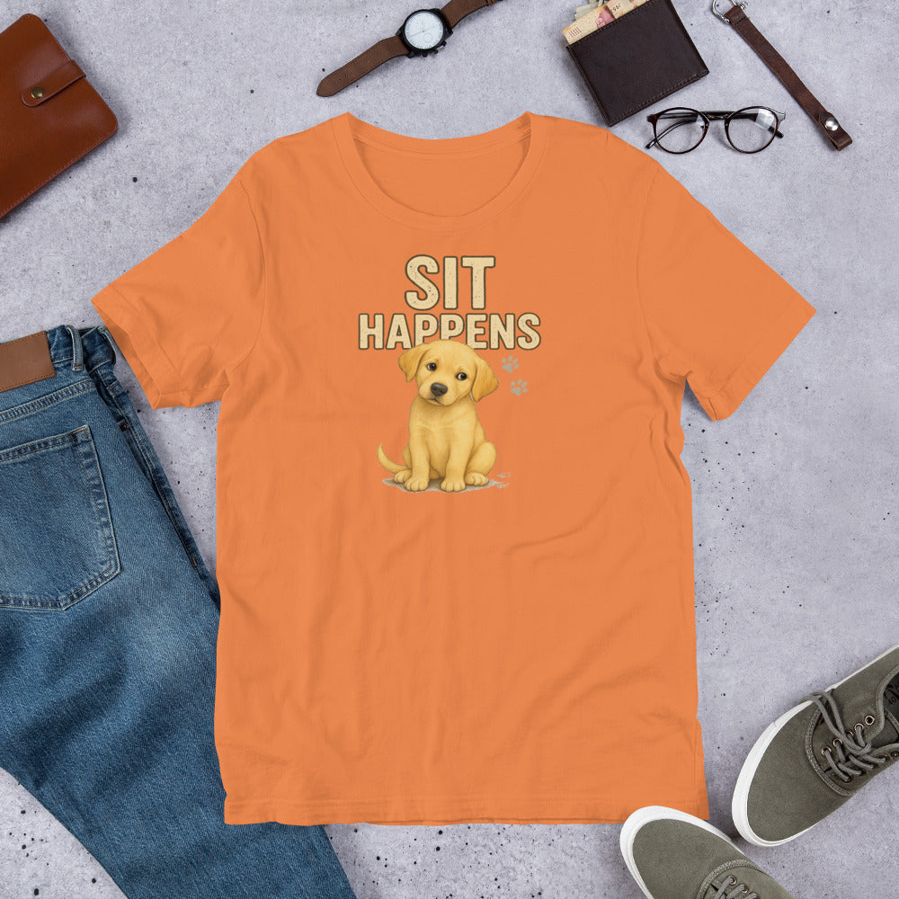 "Sit Happens " – Fun Labrador T-Shirt Orange t-shirt with a dog graphic and 'Sit Happens' text on a concrete surface with jeans, shoes, and accessories.