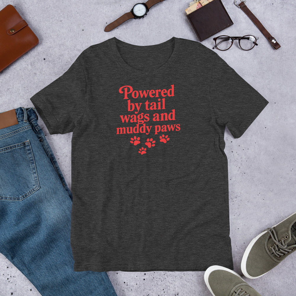 "Powered By Tail Wags And Muddy Paws" - Fun Labrador T-Shirt Dark gray t-shirt with red text and paw prints on a concrete surface with jeans, shoes, and accessories.