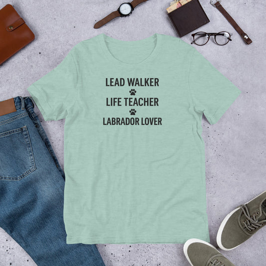 T-shirt with black text that reads 'Lead Walker, Life Teacher, Labrador Lover' with small paw print icons, laid out flat with jeans, sneakers, and accessories.