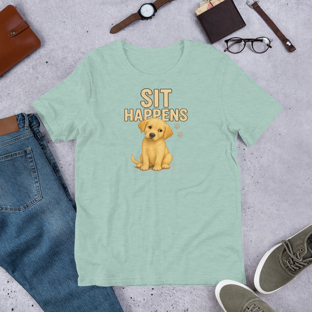 "Sit Happens " – Fun Labrador T-Shirt Light green t-shirt with a puppy graphic and 'SIT HAPPENS' text on a gray surface with jeans, shoes, and accessories.