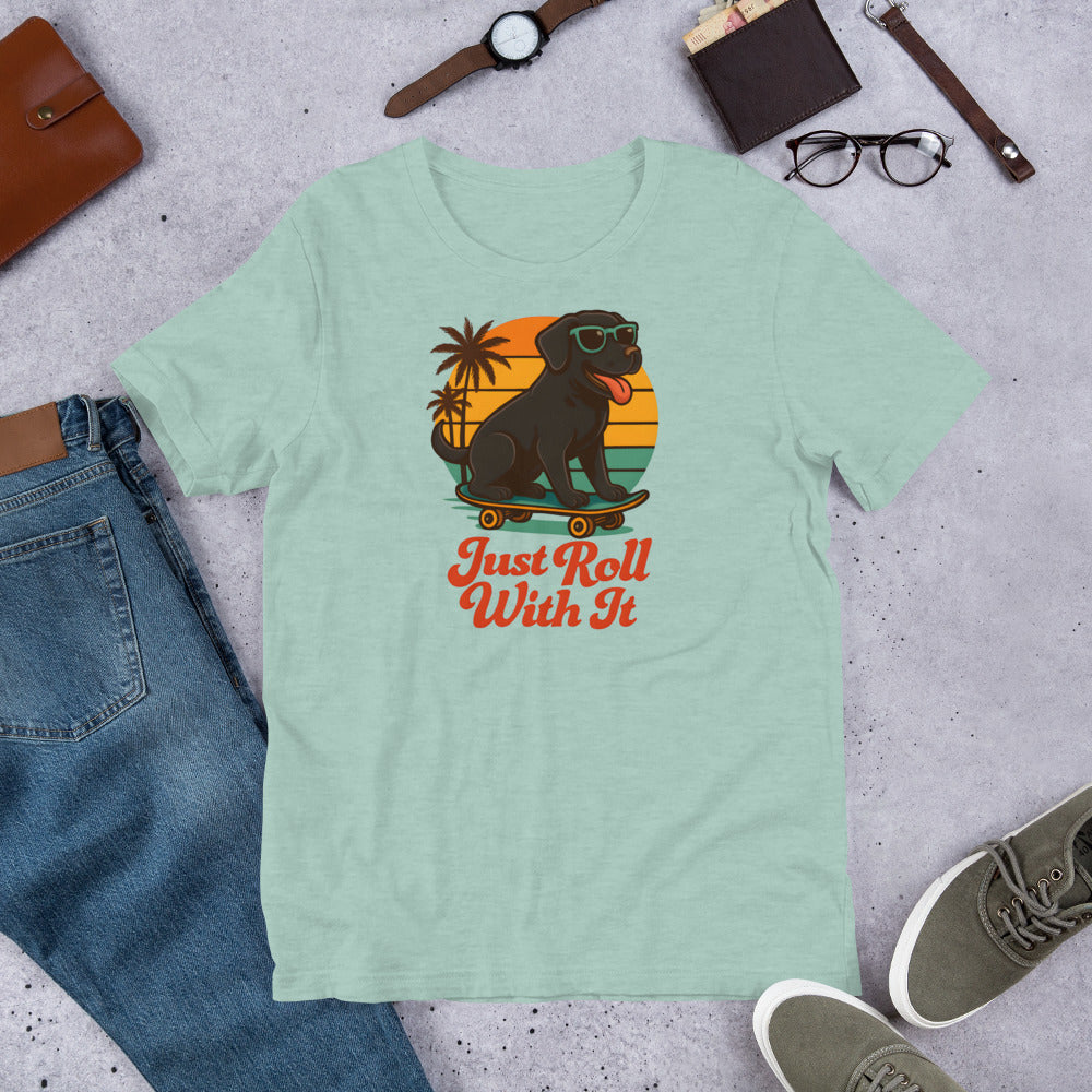 "Just Roll With It" - Black Labrador – Fun Labrador T-Shirt Light green t-shirt with a dog on a skateboard graphic and 'Just Roll With It' text, surrounded by jeans, shoes, and accessories.