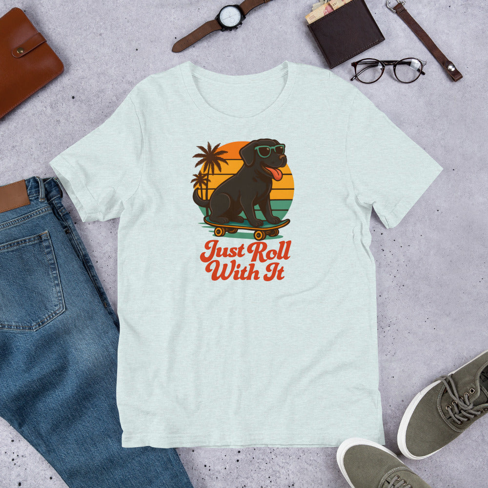 "Just Roll With It" - Black Labrador – Fun Labrador T-Shirt Light blue t-shirt with a dog graphic and 'Just Roll With It' text, surrounded by jeans, shoes, and accessories on a gray surface.