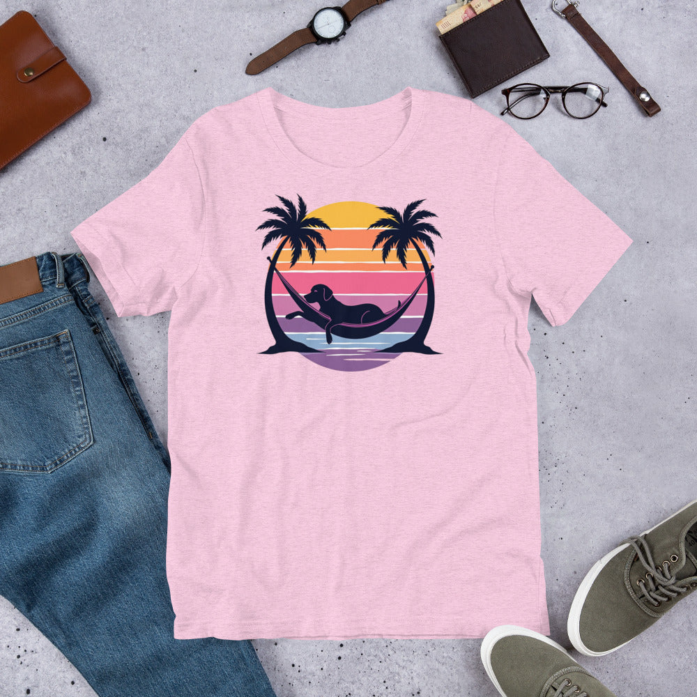 "Labrador In Paradise " – Fun Labrador T-Shirt Pink t-shirt with a graphic design of a mermaid and palm trees on a sunset background, placed on a concrete surface with jeans, shoes, and accessories.