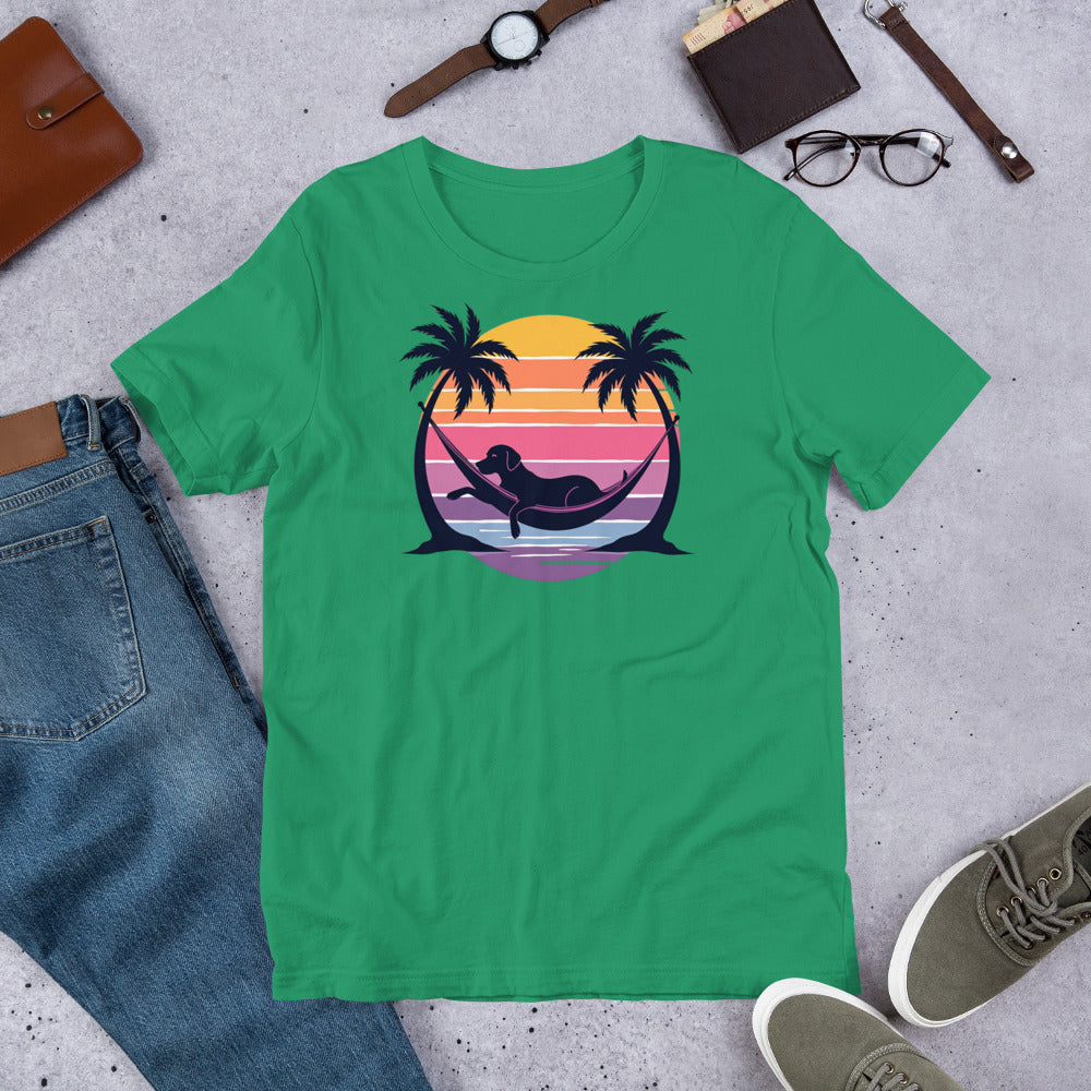 "Labrador In Paradise " – Fun Labrador T-Shirt Green t-shirt with a graphic design of a hammock between palm trees and a sunset, placed on a concrete surface with jeans, shoes, and accessories.