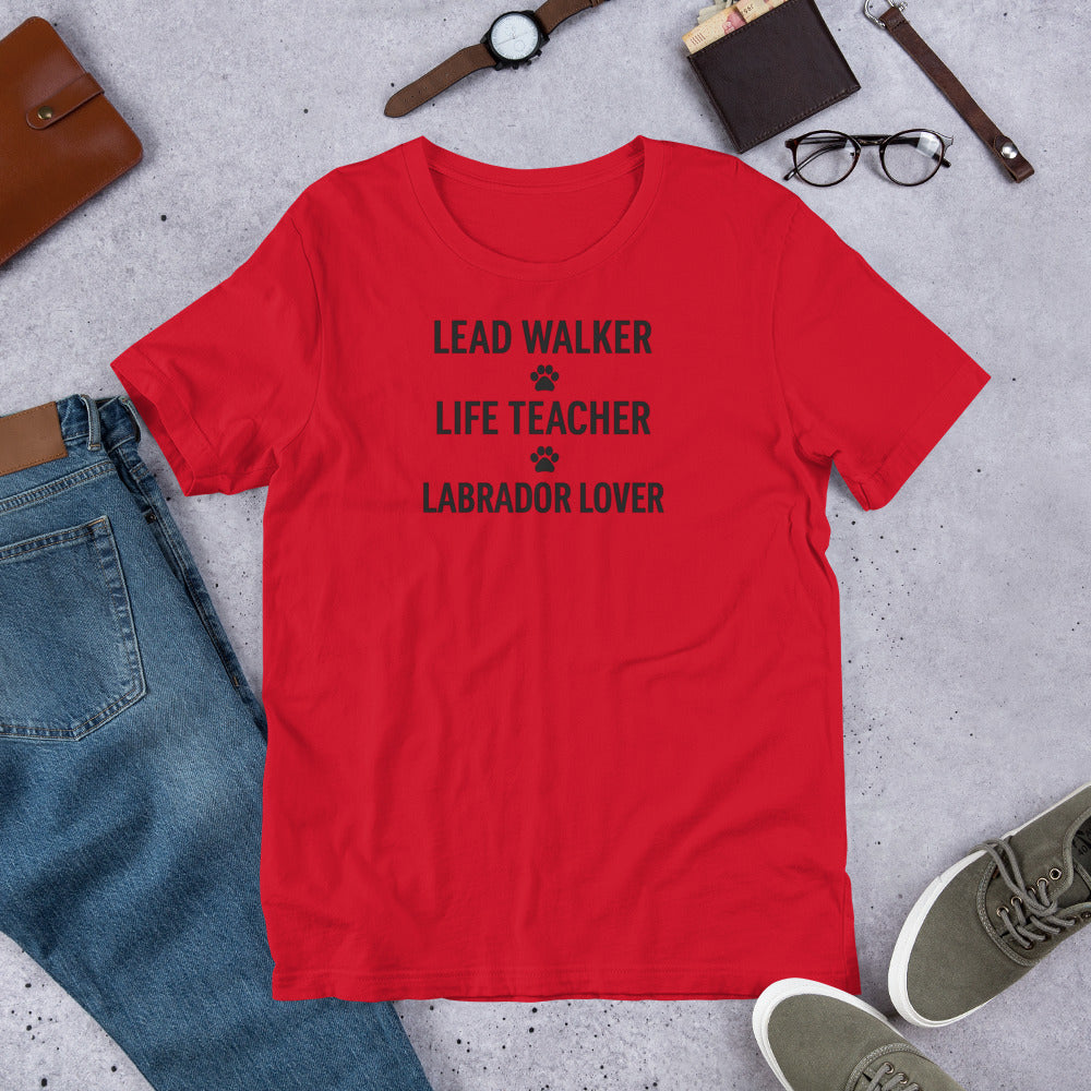 T-shirt with black text that reads 'Lead Walker, Life Teacher, Labrador Lover' with small paw print icons, laid out flat with jeans, sneakers, and accessories.