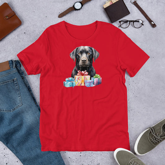"Black Lab With Presents " – Fun Labrador T-Shirt Red t-shirt with a dog and gift boxes design, surrounded by jeans, shoes, and accessories on a concrete surface.