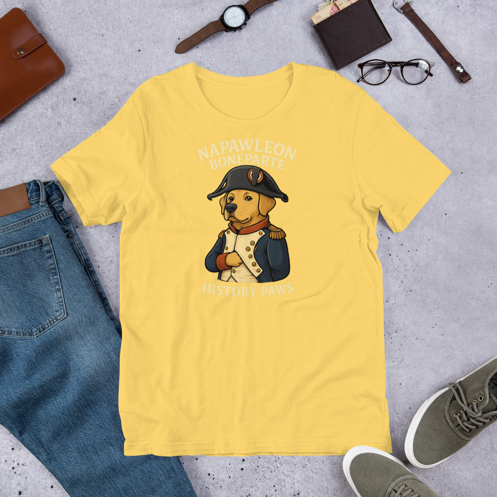 "Napawleon Boneparte" -Fun Labrador T-Shirt  Yellow t-shirt with a bear in a Napoleon costume graphic, surrounded by jeans, shoes, and accessories on a concrete surface.