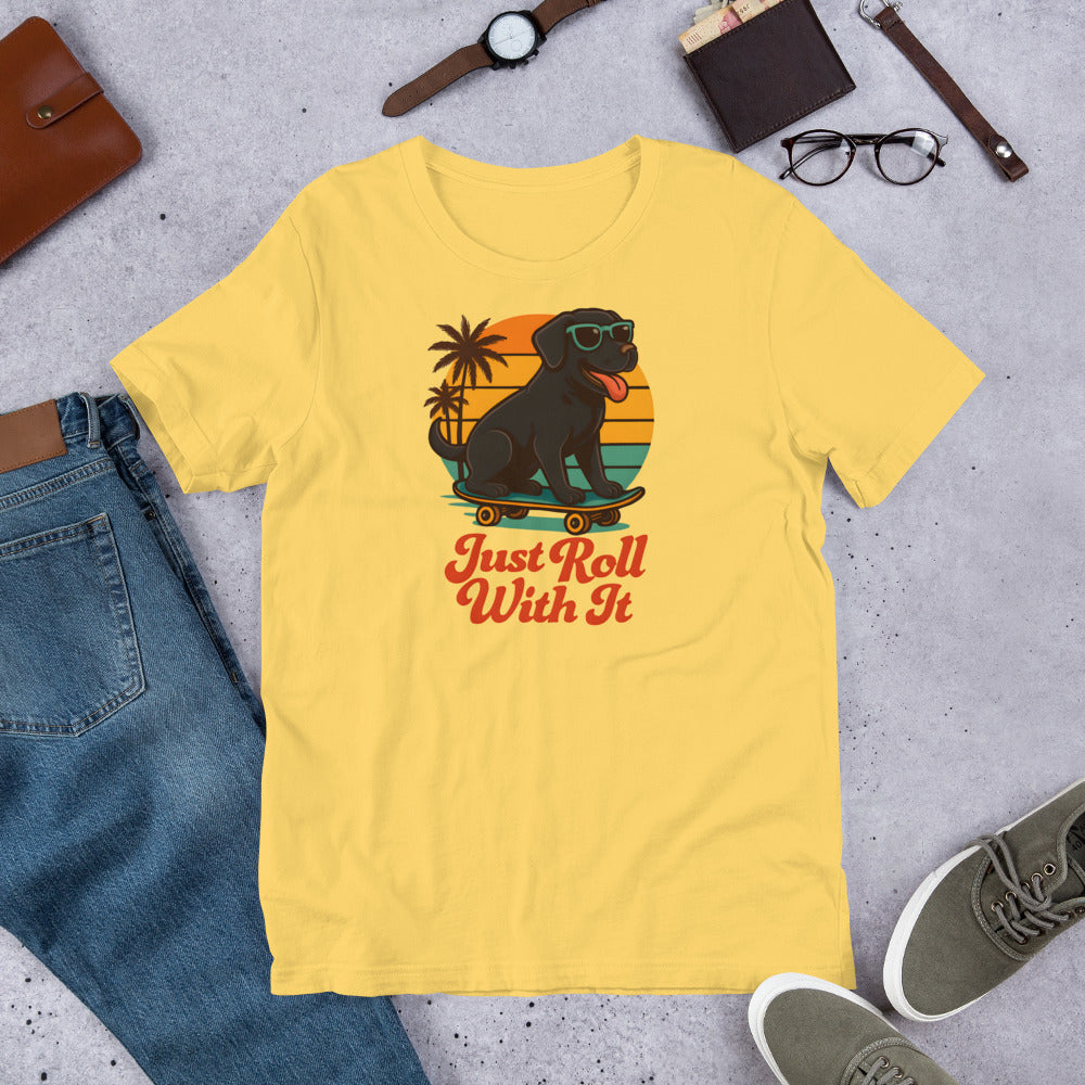 "Just Roll With It "  - Yellow Lab – Fun Labrador T-Shirt Yellow t-shirt with a dog on a skateboard graphic and 'Just Roll With It' text, surrounded by casual items on a concrete surface.